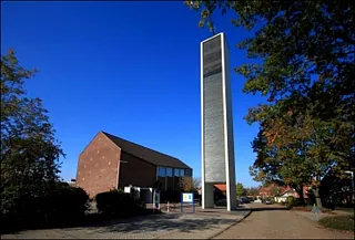 Moderne Kirche mit hohem, schlanken Glockenturm unter blauem Himmel.